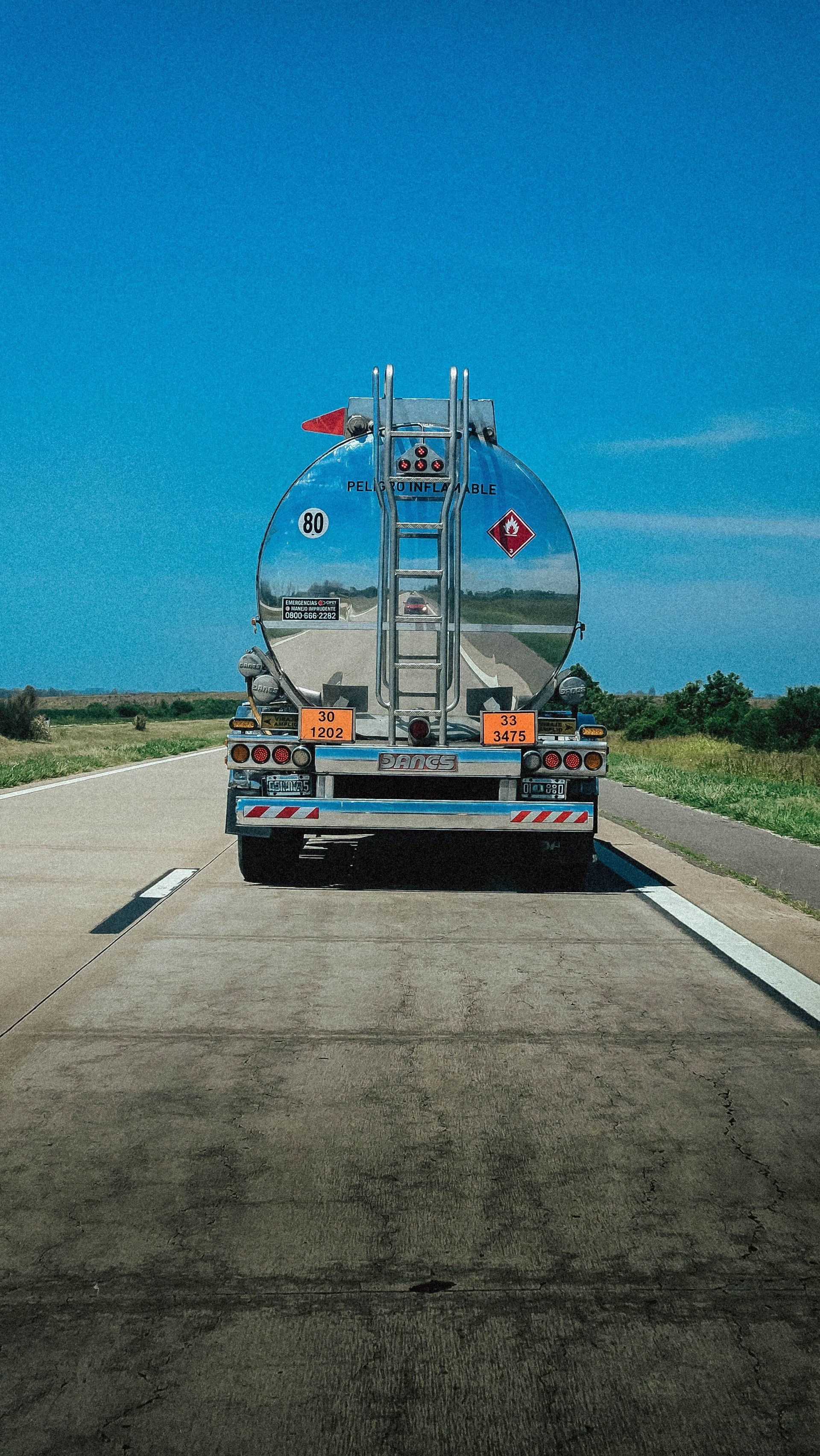 A fuel tanker truck travels along a highway under clear blue skies in Argentina.