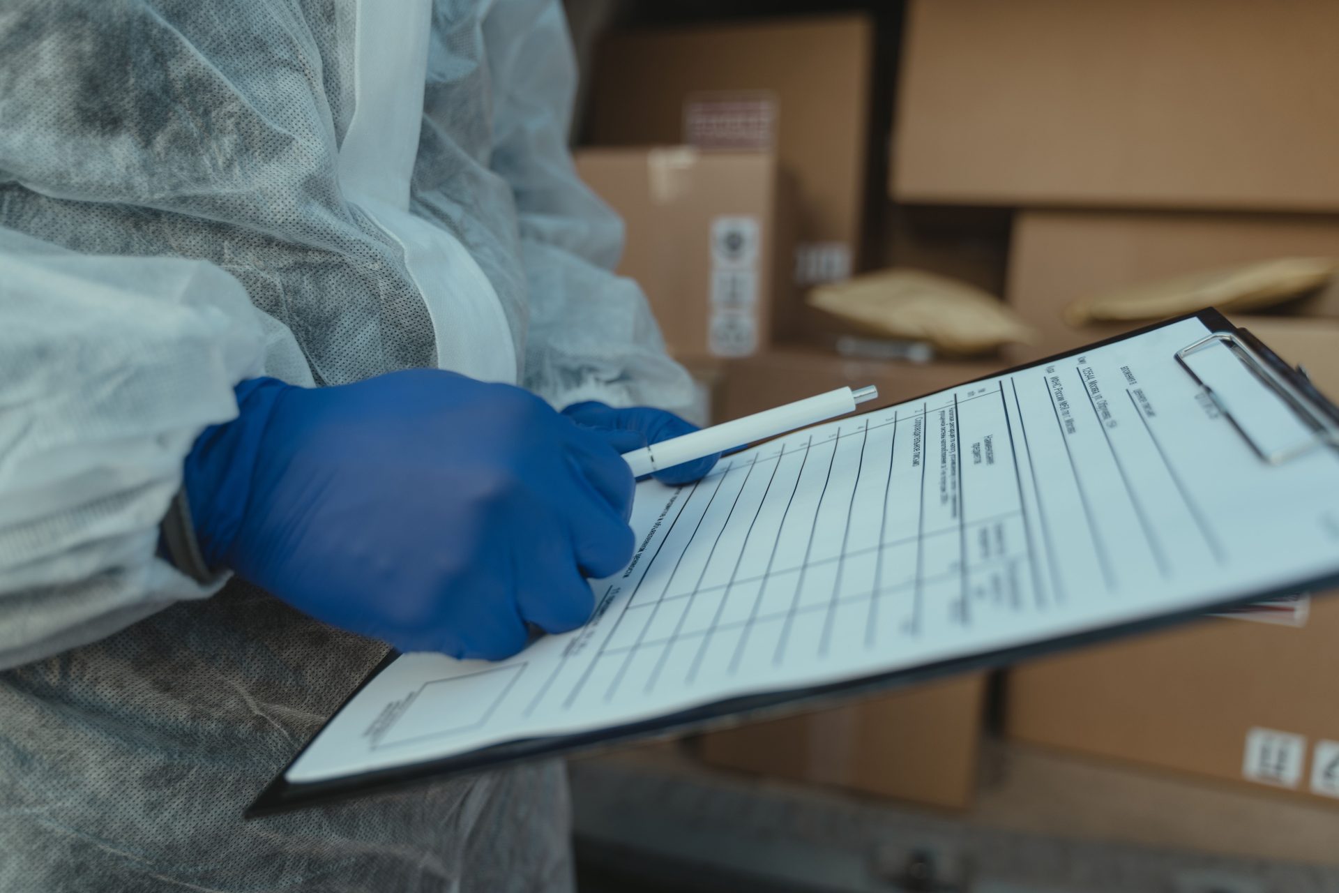 A courier wearing protective equipment writes on a clipboard among packages.