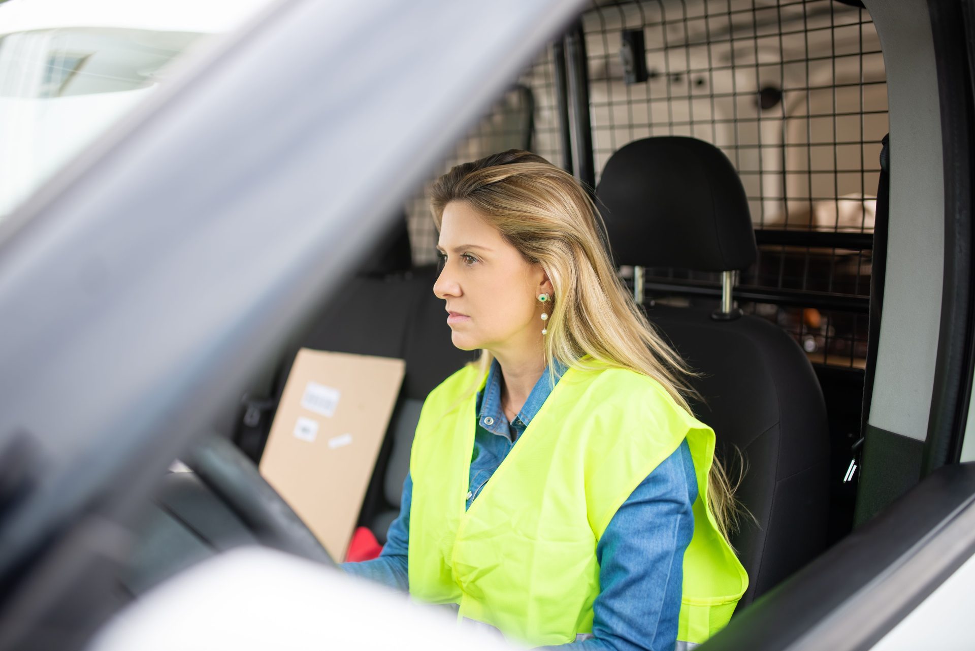 Caucasian female courier delivering packages in a van, wearing a safety vest.